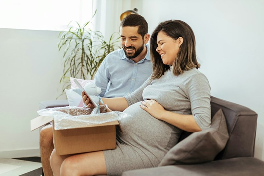 Couple expecting a new baby sitting on a lounge, with a Beechville Lane Gift Hamper