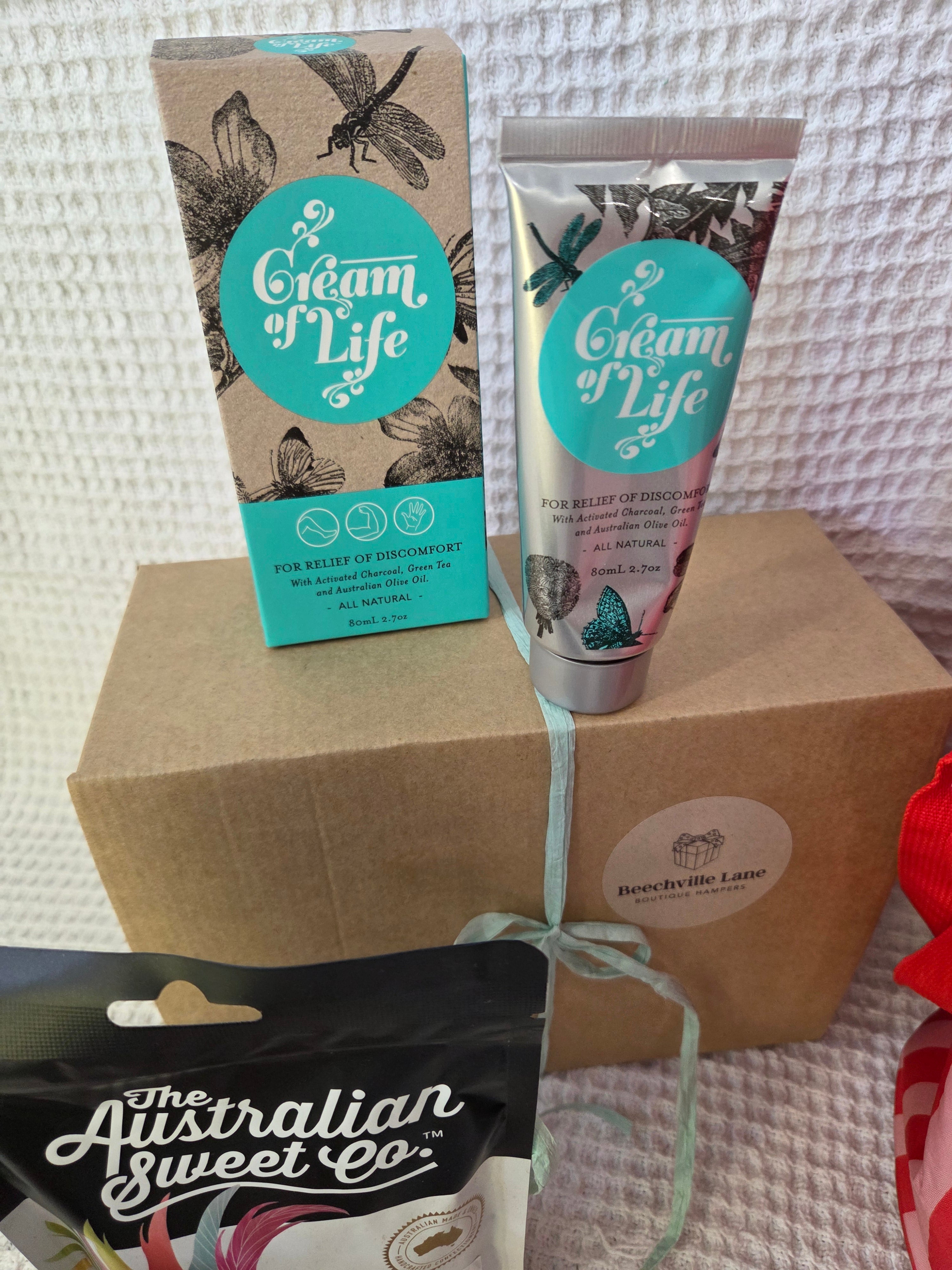 'Cream of Life' on a textured surface with a 'Australian Sweet Co.' product in the foreground. Hamper for her