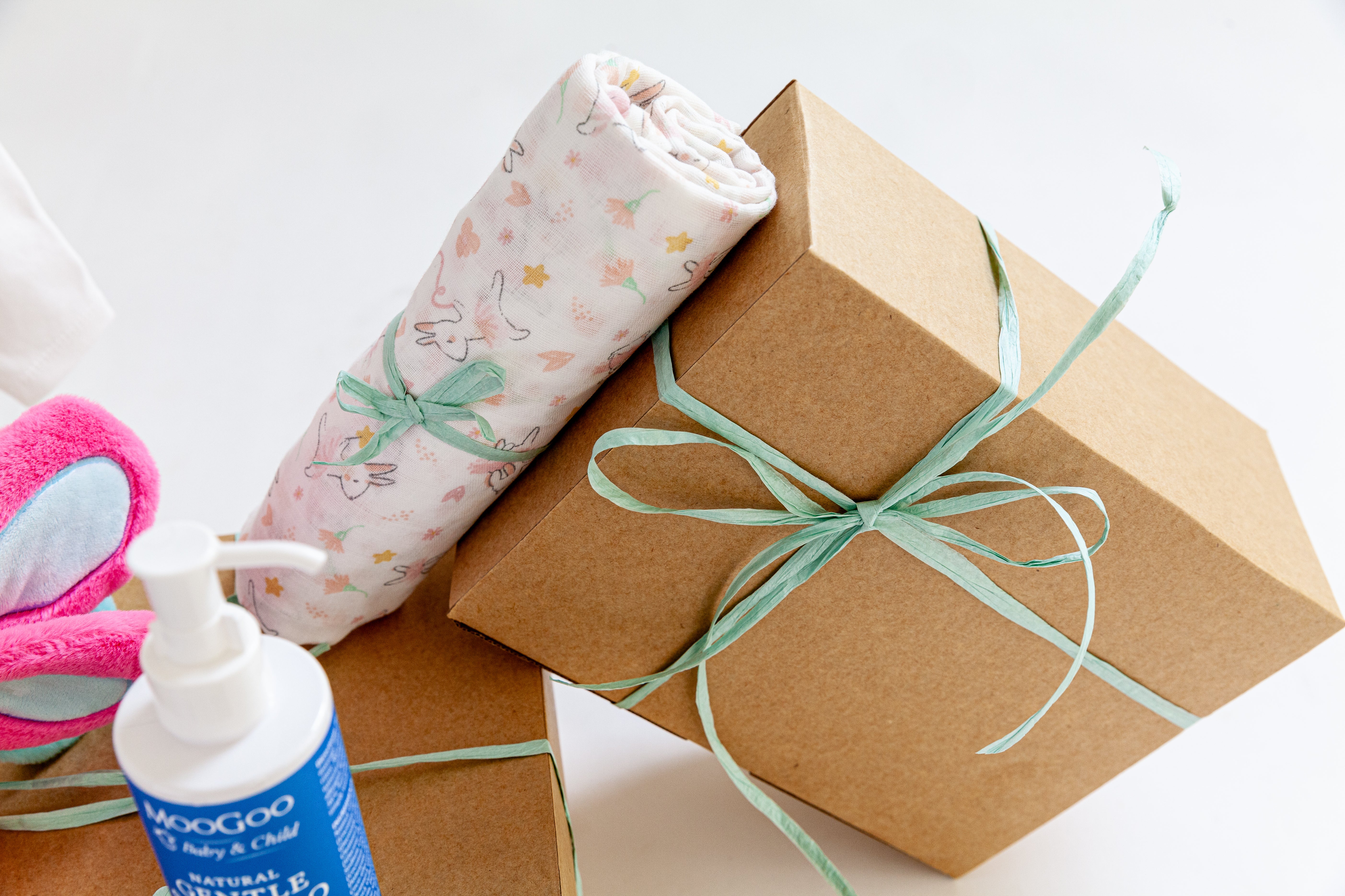 Gift box with brown paper and green ribbon, baby blanket, and bottle on a white background. Corporate maternity hamper Australia